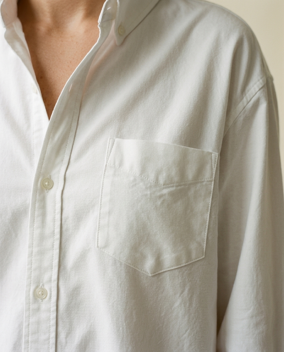 Close-up of the left chest patch pocket on the bride's white cotton Oxford shirt, showing the angled hem and tonal topstitching