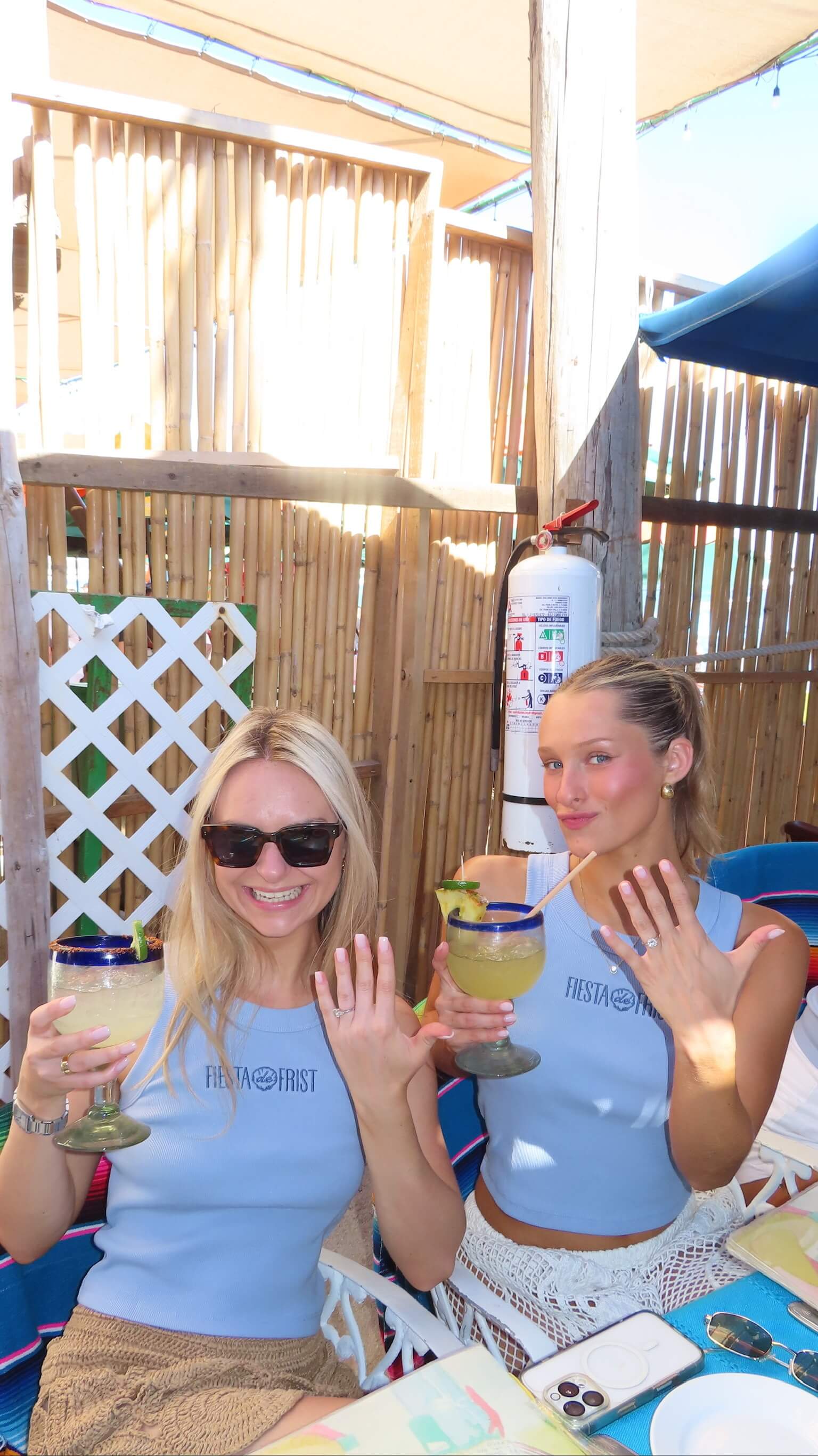 Two women in blue shirts holding drinks at an outdoor setting